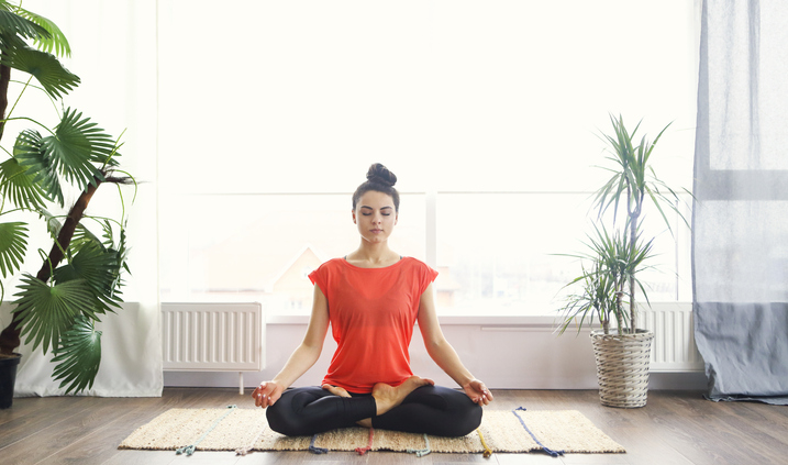 Attractive young brunette woman exercising and sitting in yoga lotus position while resting at home