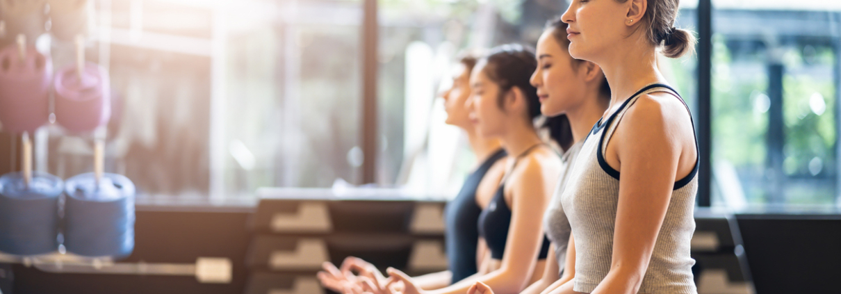 Group of Multi ethics people learning Yoga class in fitness club. Female Caucasian instructor leading Meditate sitting Yoga pose, students follow behind. Yoga for health, wellness and sport concept.