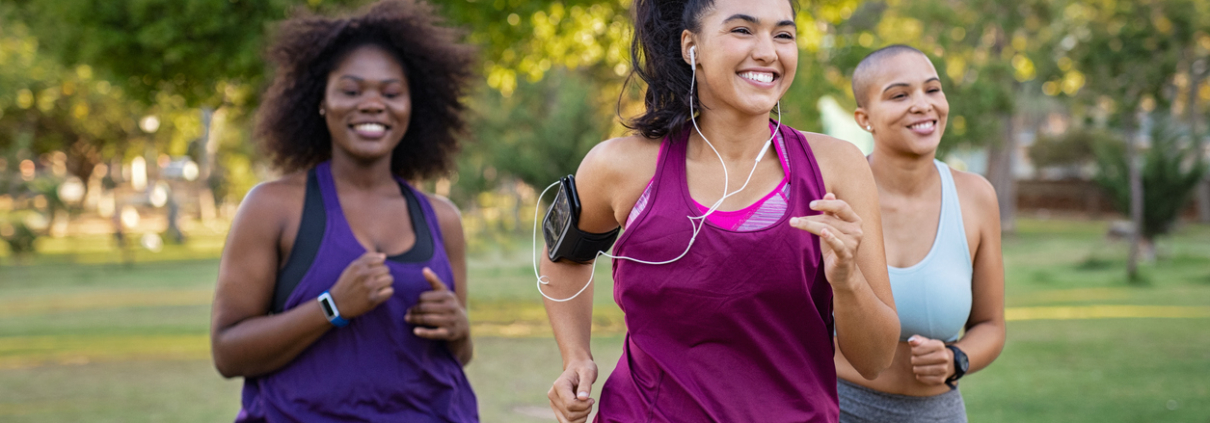 Group of curvy girls friends jogging together at park. Beautiful smiling young women running at the park on a sunny day. Female runners listening to music while jogging.