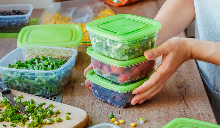 Close up of woman preparing plastic food boxes with fresh green onion, strawberry and blackberry for freezing on the wooden table.