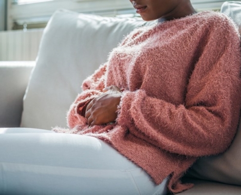 A woman in a sweater sits on her sofa with both hands on her abdomen