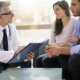 A male doctor with a medical chart sits across from a couple discussing fertility options.