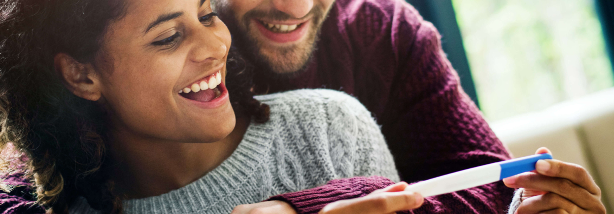 A happy couple embraces and smiles at a positive pregnancy test