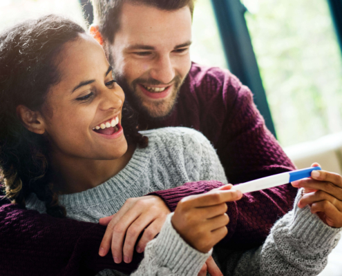 A happy couple embraces and smiles at a positive pregnancy test