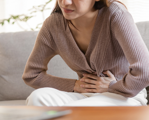 A woman sitting on a couch gripping her abdomen in pain with both hands.