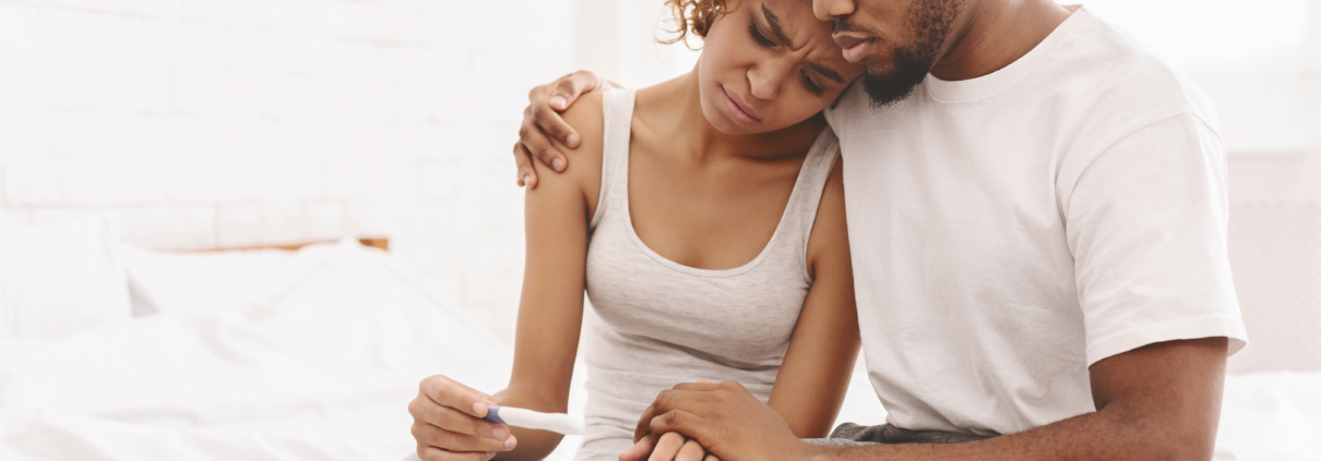 Infertility problem. Upset african american couple sitting on bed with negative pregnancy test result, free space