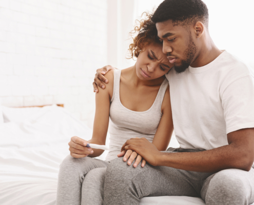 Black couple sitting together looking disappointed while holding a negative pregnancy test