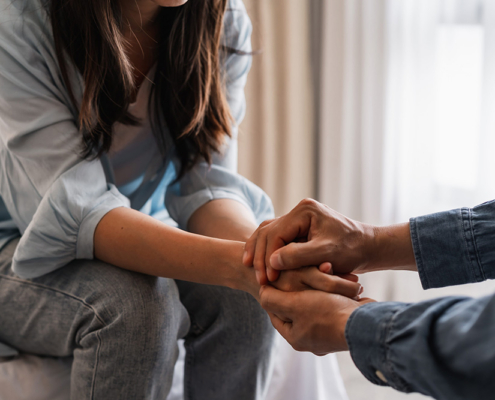 A young man with a hand on the shoulder of distressed woman who is sitting on couch. He is offering comfort and support in a home setting.