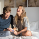 A happy couple sitting on the bed together, looking at a pregnancy test, smiling with joy and anticipation.