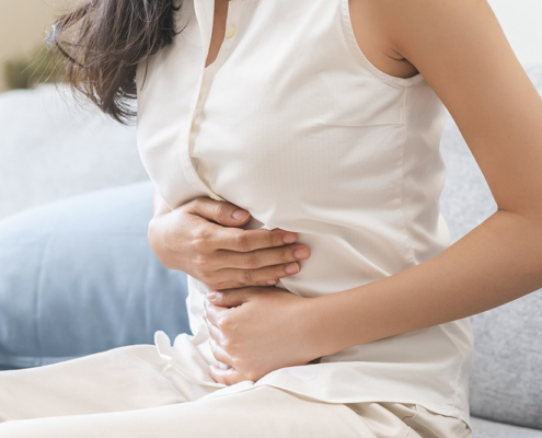 Woman sitting on a sofa, holding her abdomen with both hands