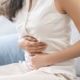 Woman sitting on a sofa, holding her abdomen with both hands