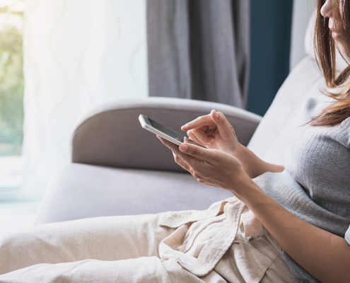 Woman using a smartphone while sitting on a sofa near a window.