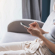Woman using a smartphone while sitting on a sofa near a window.